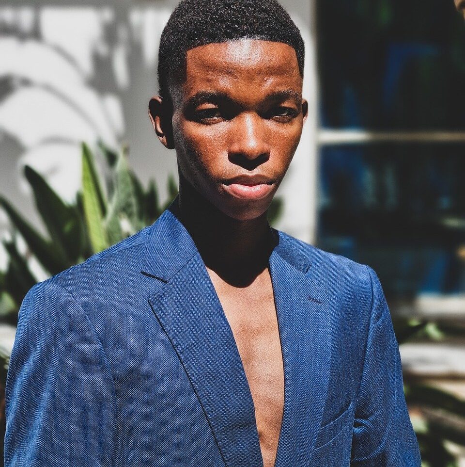 close-up portrait, black male model, fierce stare, intense expression, blue suit, fashion close-up, dominant look, editorial headshot, bold gaze, male model close-up, high fashion, strong facial expression, fashion editorial, confident face, stylish man